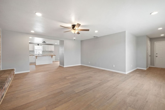 unfurnished living room featuring light wood-style flooring, recessed lighting, a sink, a ceiling fan, and baseboards