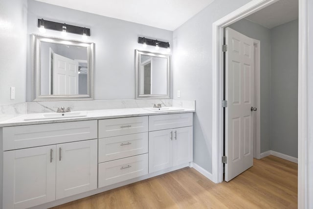 full bath featuring double vanity, wood finished floors, a sink, and baseboards