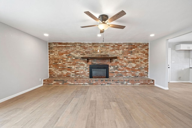 unfurnished living room with ceiling fan, light wood finished floors, a brick fireplace, and baseboards