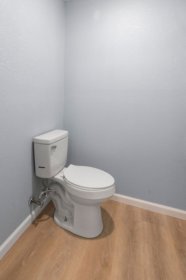 half bath featuring wood finished floors, toilet, and baseboards