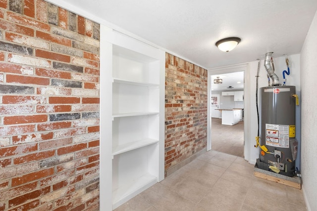 hall with built in shelves, gas water heater, and brick wall