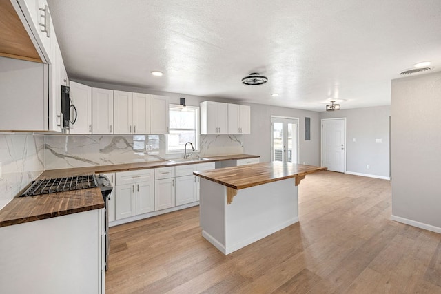 kitchen with butcher block counters, a sink, white cabinetry, and light wood-style floors