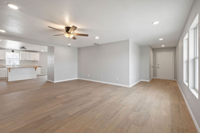 unfurnished living room with a sink, light wood-style flooring, baseboards, and ceiling fan