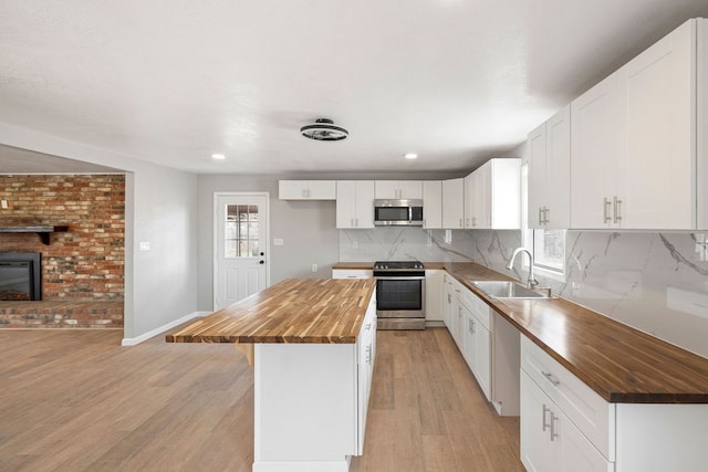 kitchen featuring butcher block countertops, a center island, white cabinets, and appliances with stainless steel finishes