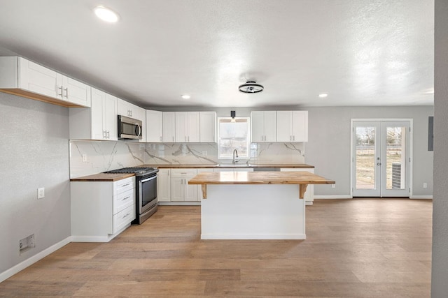 kitchen with appliances with stainless steel finishes, butcher block counters, white cabinets, and plenty of natural light