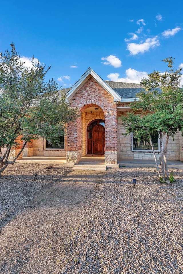 view of front of house with stone siding, brick siding, and a shingled roof