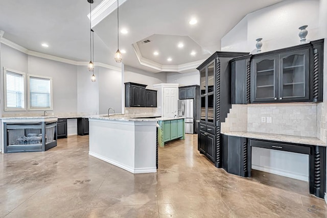 kitchen featuring stainless steel refrigerator with ice dispenser, hanging light fixtures, decorative backsplash, glass insert cabinets, and an island with sink