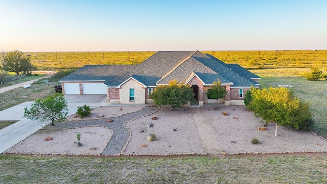 view of front of home featuring an attached garage, concrete driveway, and a rural view