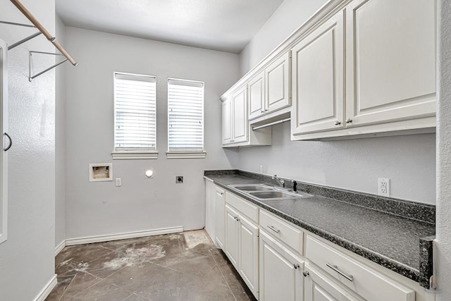 kitchen featuring dark countertops, baseboards, white cabinetry, and a sink