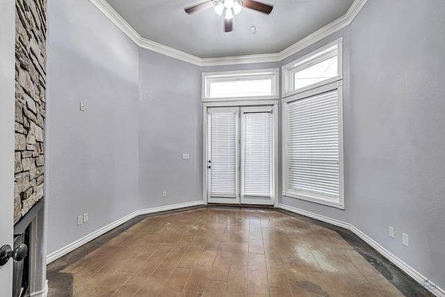 spare room with dark wood-style floors, a fireplace, ornamental molding, a ceiling fan, and baseboards