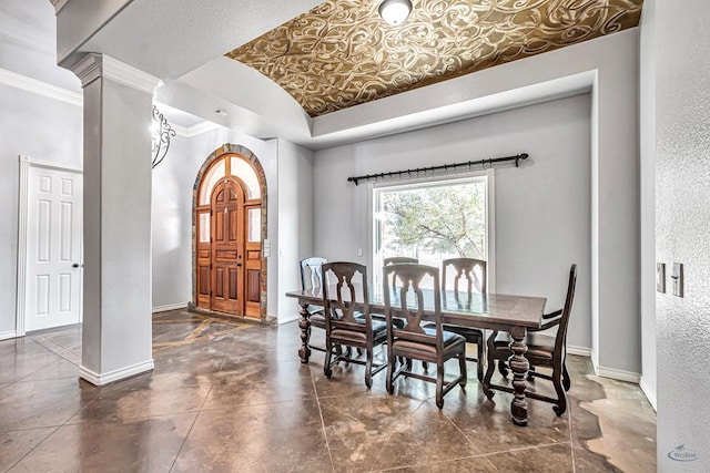 dining area with a textured wall, a tray ceiling, decorative columns, and baseboards