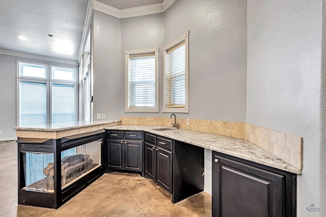 kitchen featuring a wealth of natural light, ornamental molding, light stone counters, and a sink