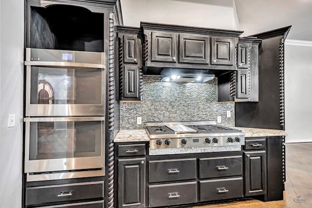 kitchen with appliances with stainless steel finishes, wall chimney range hood, light stone countertops, and tasteful backsplash