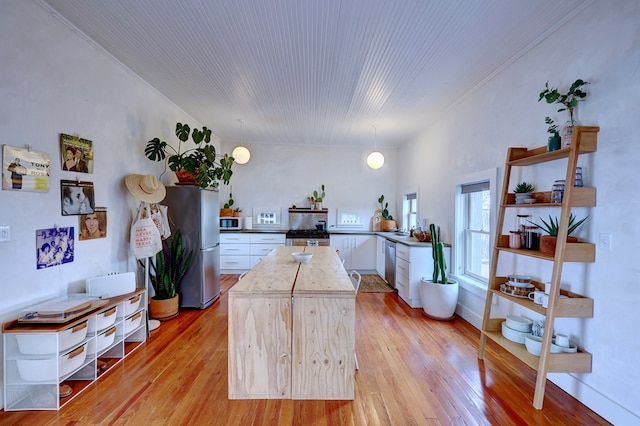 kitchen featuring pendant lighting, white cabinets, appliances with stainless steel finishes, a center island, and light wood-type flooring