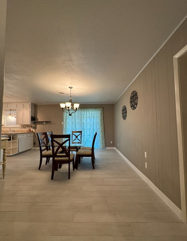 dining space featuring a textured ceiling, a chandelier, crown molding, and light hardwood / wood-style flooring