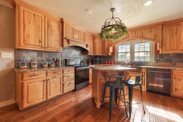 kitchen featuring appliances with stainless steel finishes, pendant lighting, wood-type flooring, a kitchen island, and custom exhaust hood