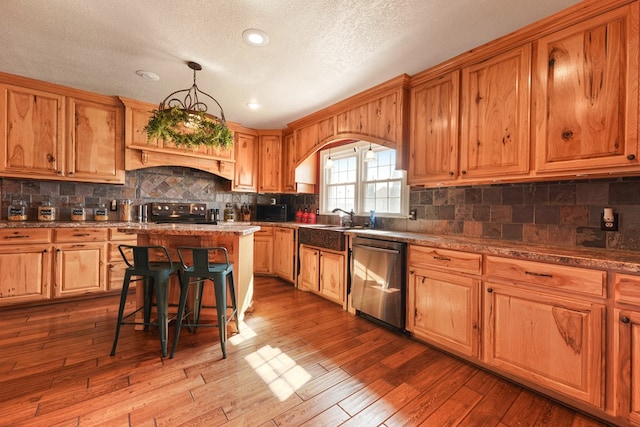 kitchen with dishwasher, a center island, light hardwood / wood-style floors, hanging light fixtures, and a breakfast bar area