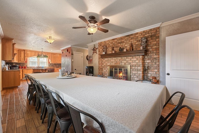 interior space featuring light wood-type flooring, a textured ceiling, ceiling fan, crown molding, and a fireplace