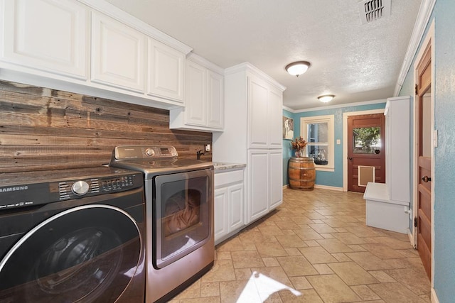 laundry room featuring washer and dryer, a textured ceiling, crown molding, and cabinets