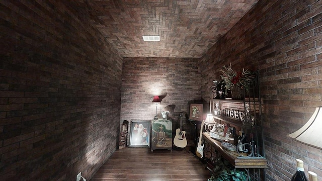 interior space with dark hardwood / wood-style floors, brick ceiling, and brick wall