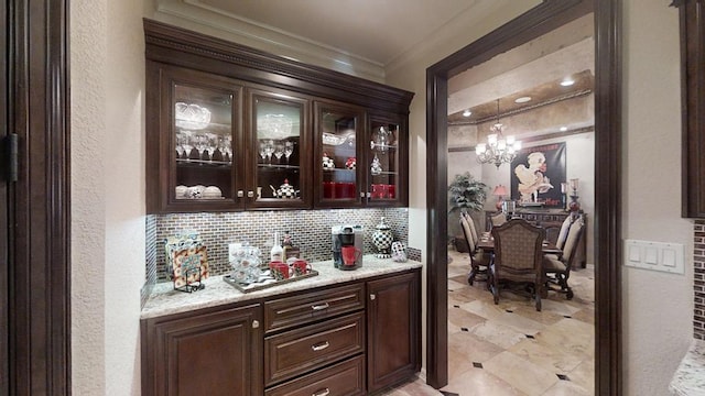 bar featuring an inviting chandelier, tasteful backsplash, light stone counters, crown molding, and decorative light fixtures