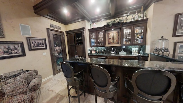 bar with beam ceiling, dark brown cabinetry, dark stone countertops, decorative backsplash, and ornamental molding