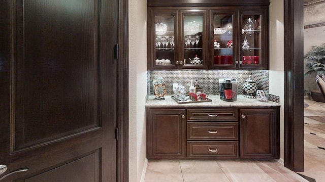 bar featuring decorative backsplash, light stone counters, and dark brown cabinets