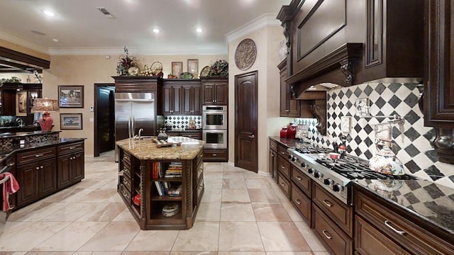 kitchen with backsplash, a kitchen island with sink, dark stone countertops, appliances with stainless steel finishes, and dark brown cabinetry