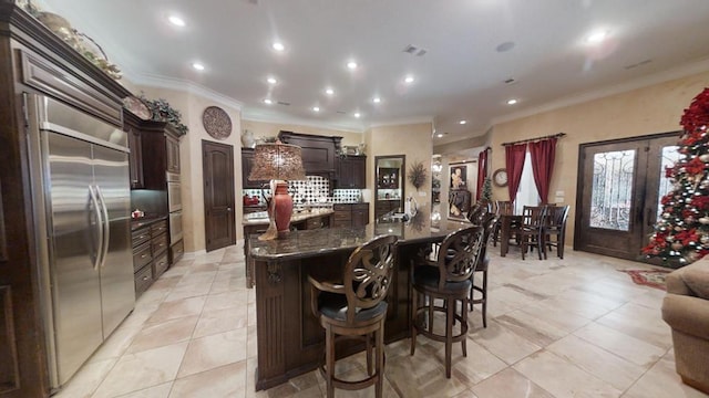 kitchen featuring stainless steel built in refrigerator, light tile patterned floors, a kitchen bar, and crown molding