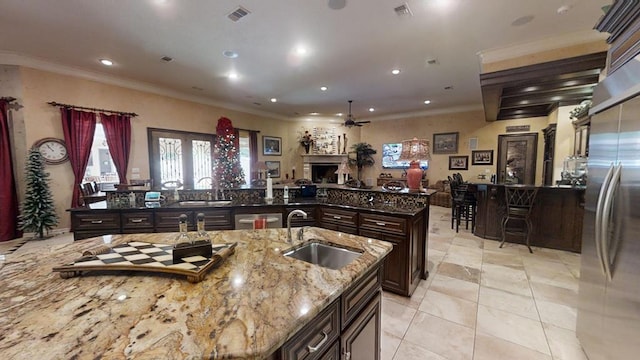 kitchen featuring light stone countertops, sink, dark brown cabinets, light tile patterned floors, and a center island with sink