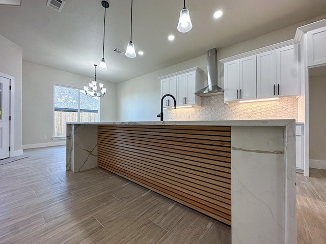 kitchen with decorative backsplash, a center island with sink, white cabinets, and wall chimney exhaust hood