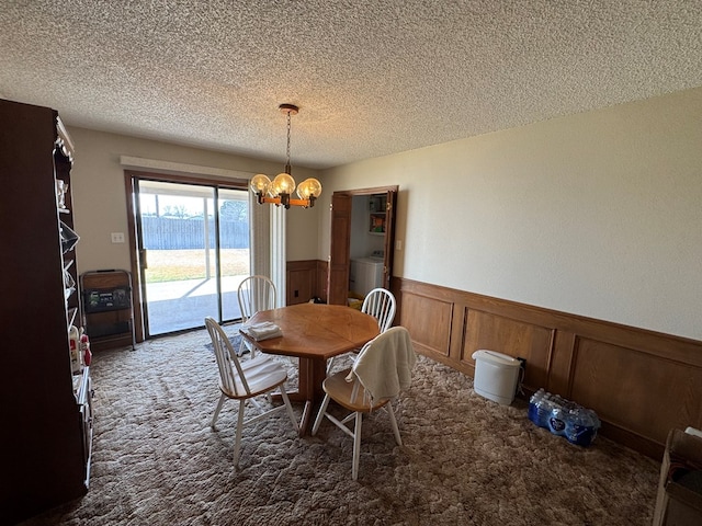 carpeted dining room with a textured ceiling, an inviting chandelier, washer / dryer, and wainscoting