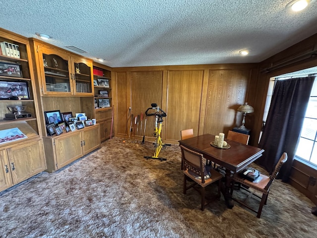 carpeted dining area with visible vents, wooden walls, and a textured ceiling