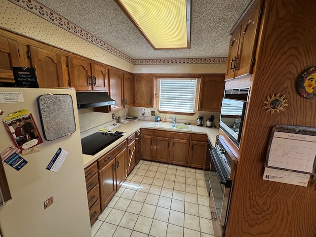 kitchen featuring under cabinet range hood, a sink, freestanding refrigerator, light countertops, and black electric stovetop