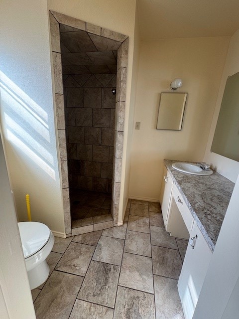 full bathroom with a tile shower, vanity, toilet, and baseboards