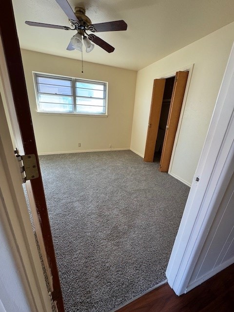 unfurnished bedroom featuring dark carpet, a ceiling fan, and baseboards