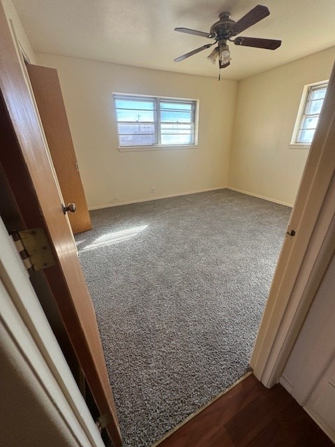 unfurnished bedroom featuring a ceiling fan, dark colored carpet, multiple windows, and baseboards