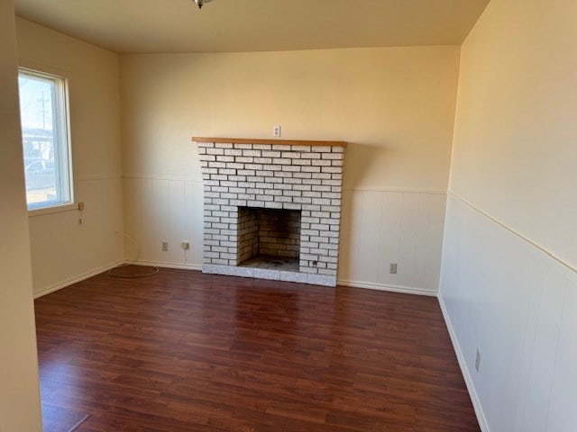 unfurnished living room featuring a brick fireplace, dark wood-style floors, and wainscoting