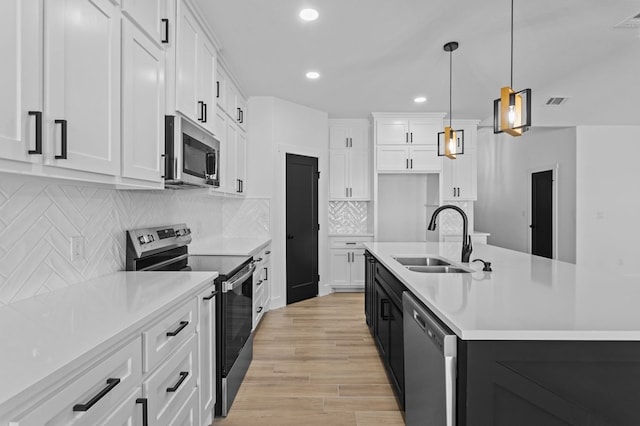 kitchen featuring appliances with stainless steel finishes, decorative light fixtures, a center island with sink, and white cabinets