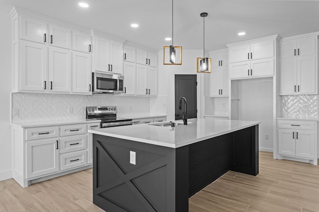 kitchen with white cabinetry, sink, stainless steel appliances, and a center island with sink