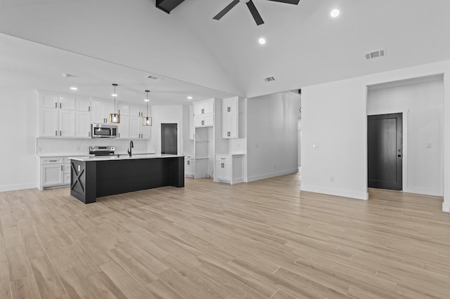 kitchen featuring appliances with stainless steel finishes, a kitchen island with sink, hanging light fixtures, white cabinetry, and light hardwood / wood-style floors