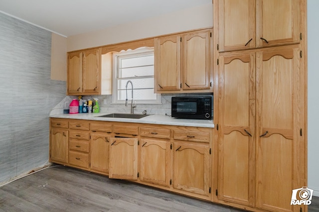 kitchen featuring light wood finished floors, a sink, light countertops, black microwave, and backsplash