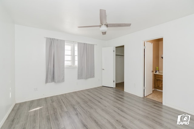 unfurnished bedroom featuring ensuite bathroom, wood finished floors, a ceiling fan, baseboards, and a spacious closet