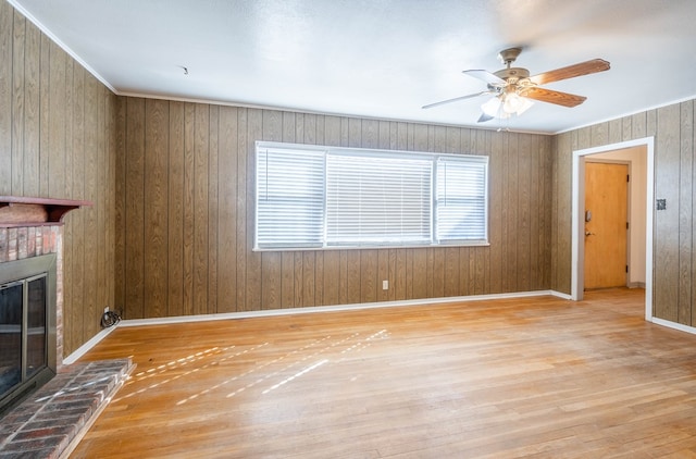 unfurnished living room with a fireplace, light hardwood / wood-style floors, wood walls, ceiling fan, and crown molding