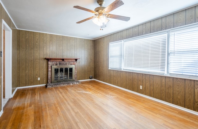 unfurnished living room featuring ceiling fan, a fireplace, hardwood / wood-style flooring, and wooden walls