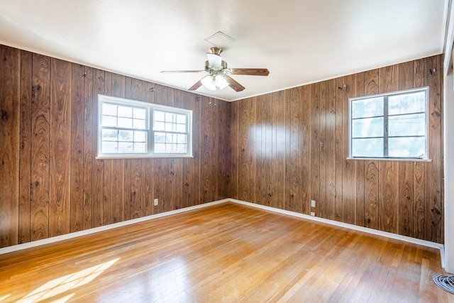 unfurnished room with ceiling fan, light wood-type flooring, and wood walls