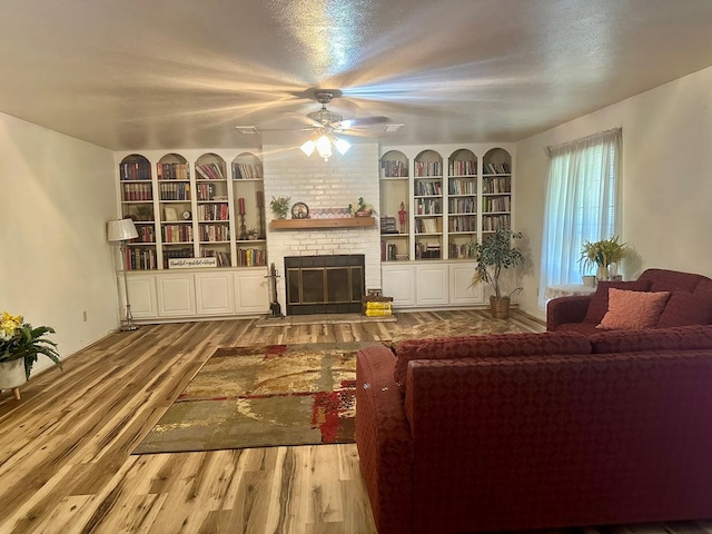 living room with ceiling fan, wood-type flooring, a textured ceiling, and a brick fireplace