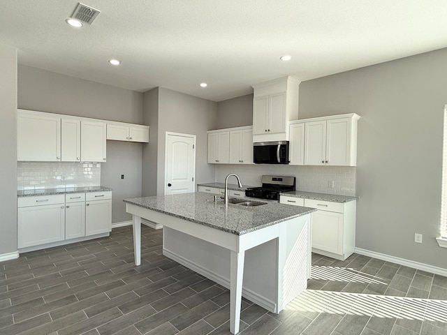 kitchen featuring light stone counters, stainless steel appliances, a kitchen island with sink, sink, and white cabinets