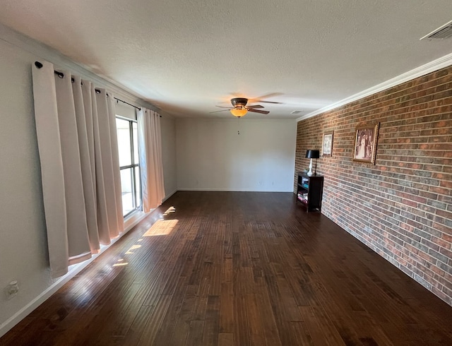 unfurnished room featuring dark wood-type flooring, ceiling fan, ornamental molding, a textured ceiling, and brick wall