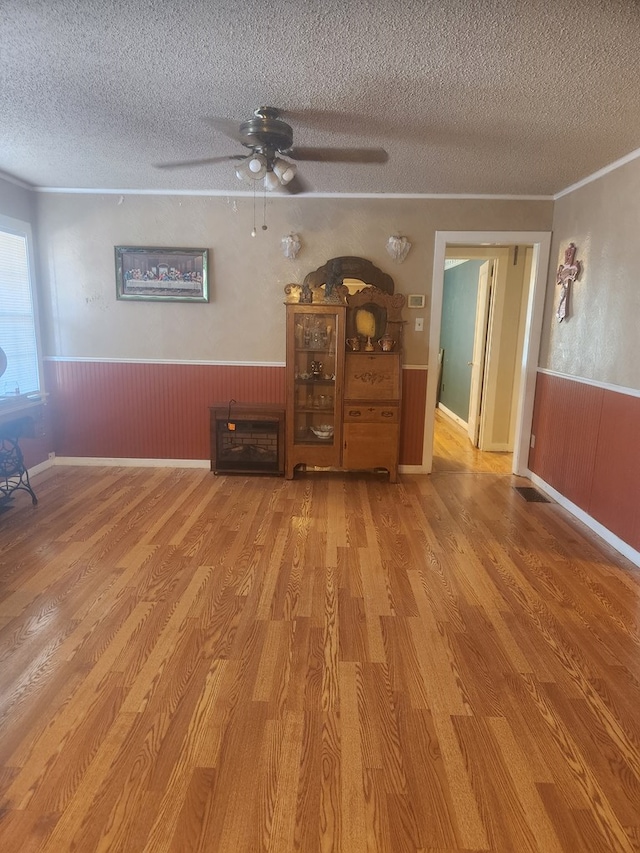 unfurnished living room featuring hardwood / wood-style floors, a textured ceiling, ceiling fan, and ornamental molding